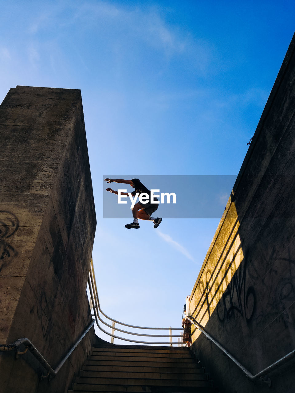 Low angle view of man jumping above steps against blue sky
