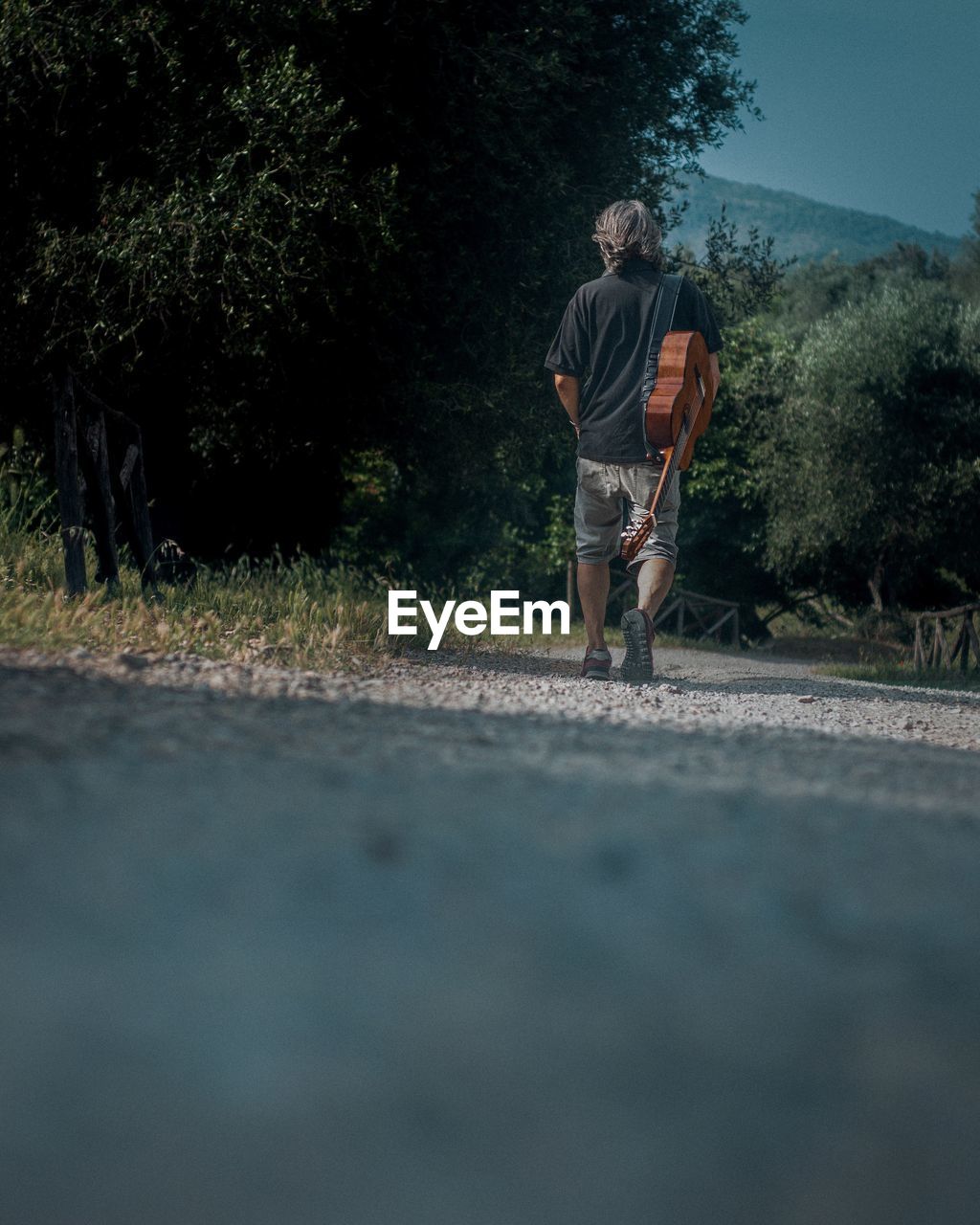 REAR VIEW OF MAN WALKING ON ROAD AMIDST TREES