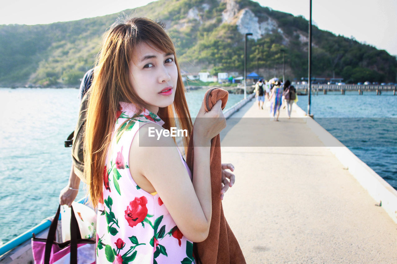 Portrait of beautiful woman standing on walkway amidst sea