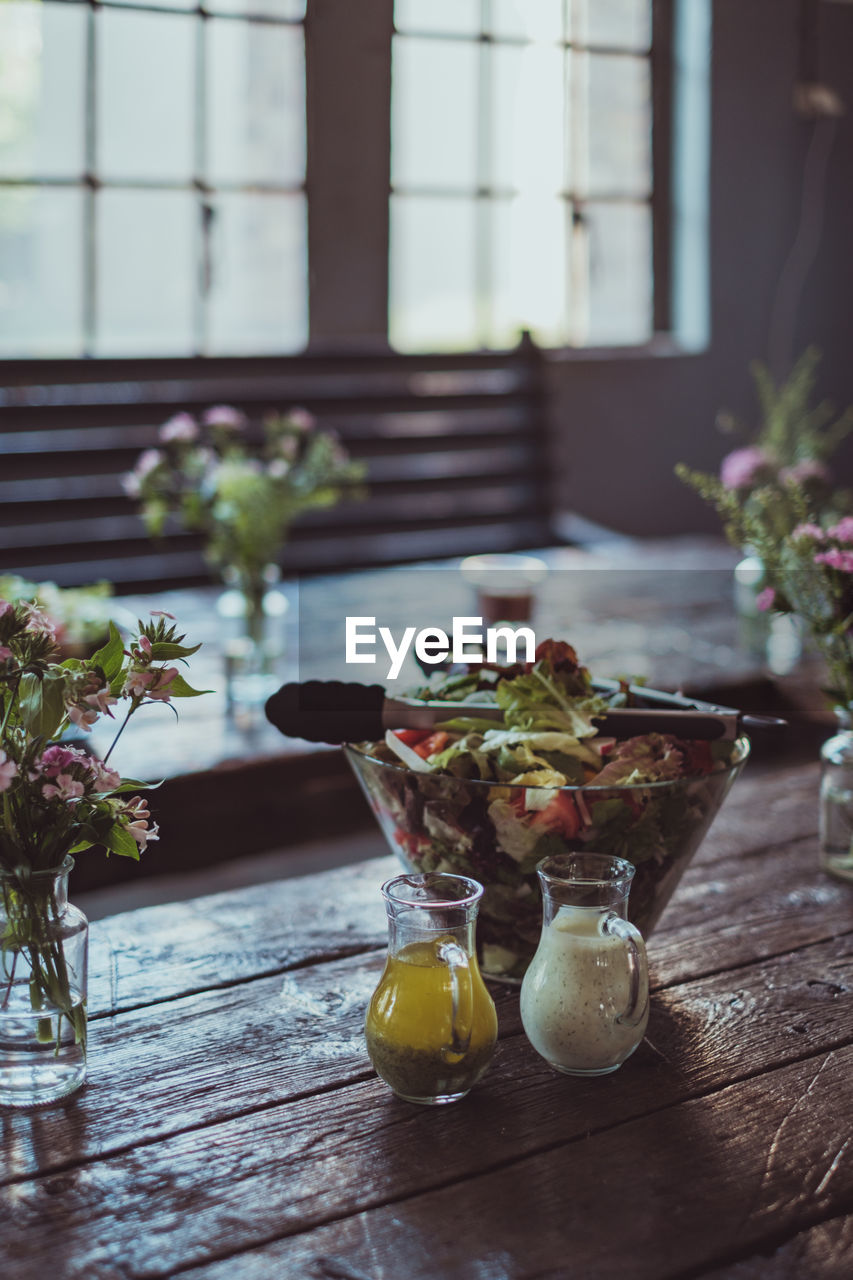 Refreshing salad and flower vase on wooden table by window