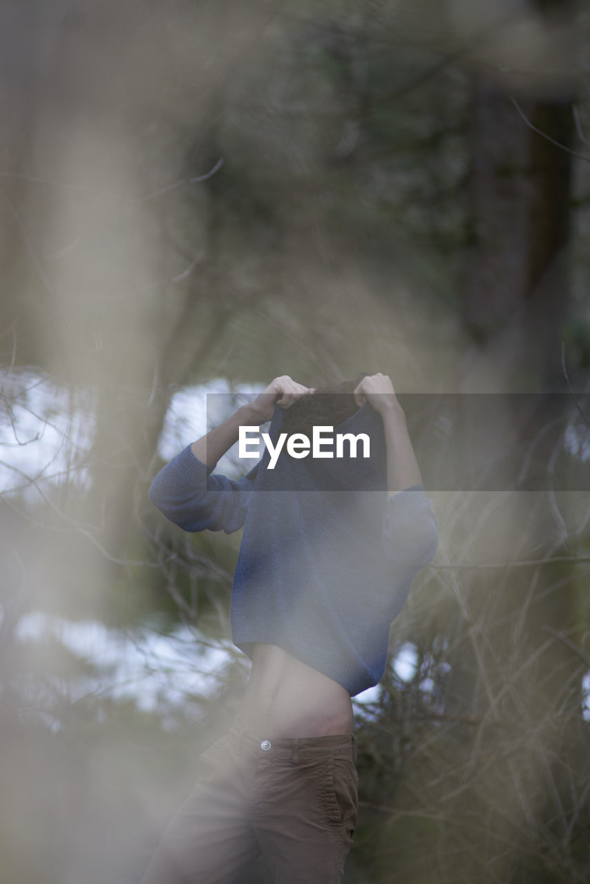 Man pulling off t-shirt while standing in forest