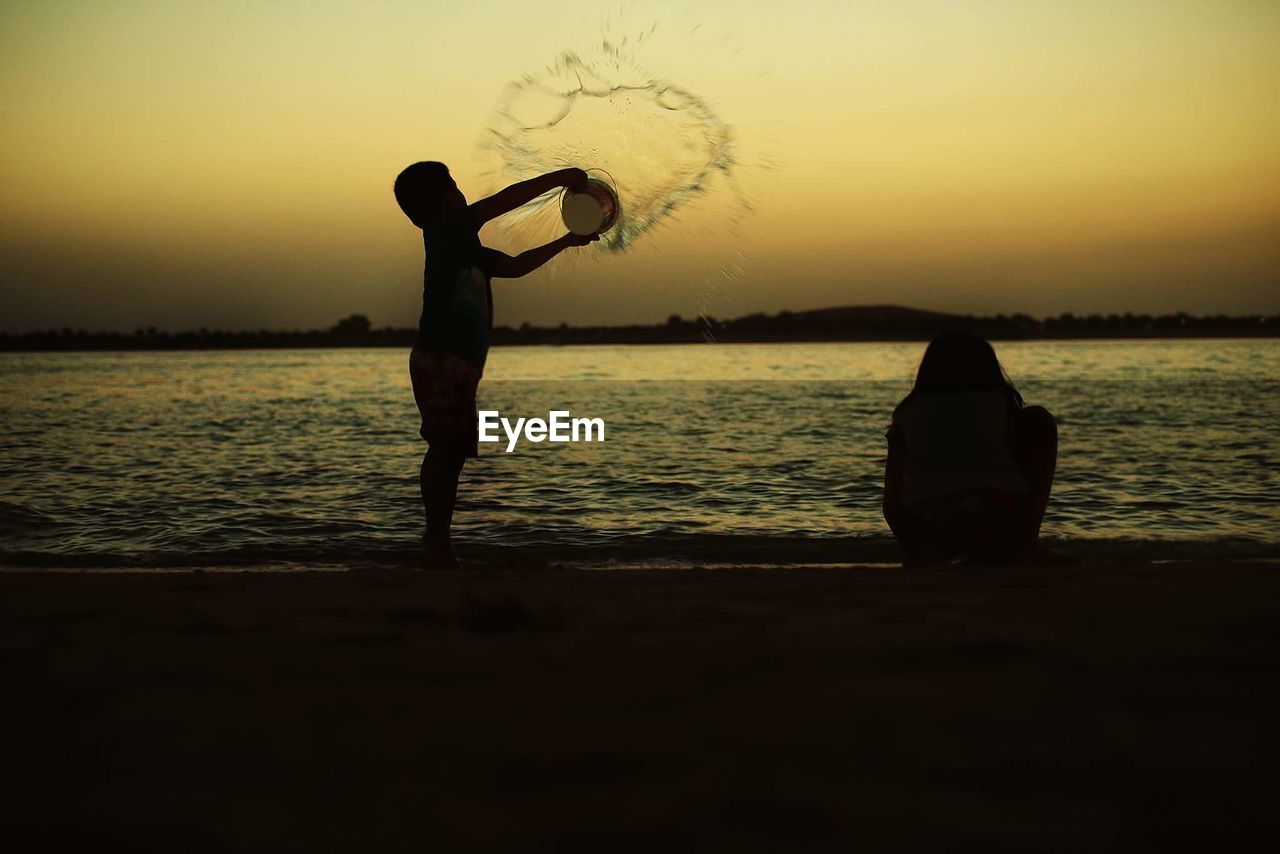 Playful siblings on shore at beach during sunset