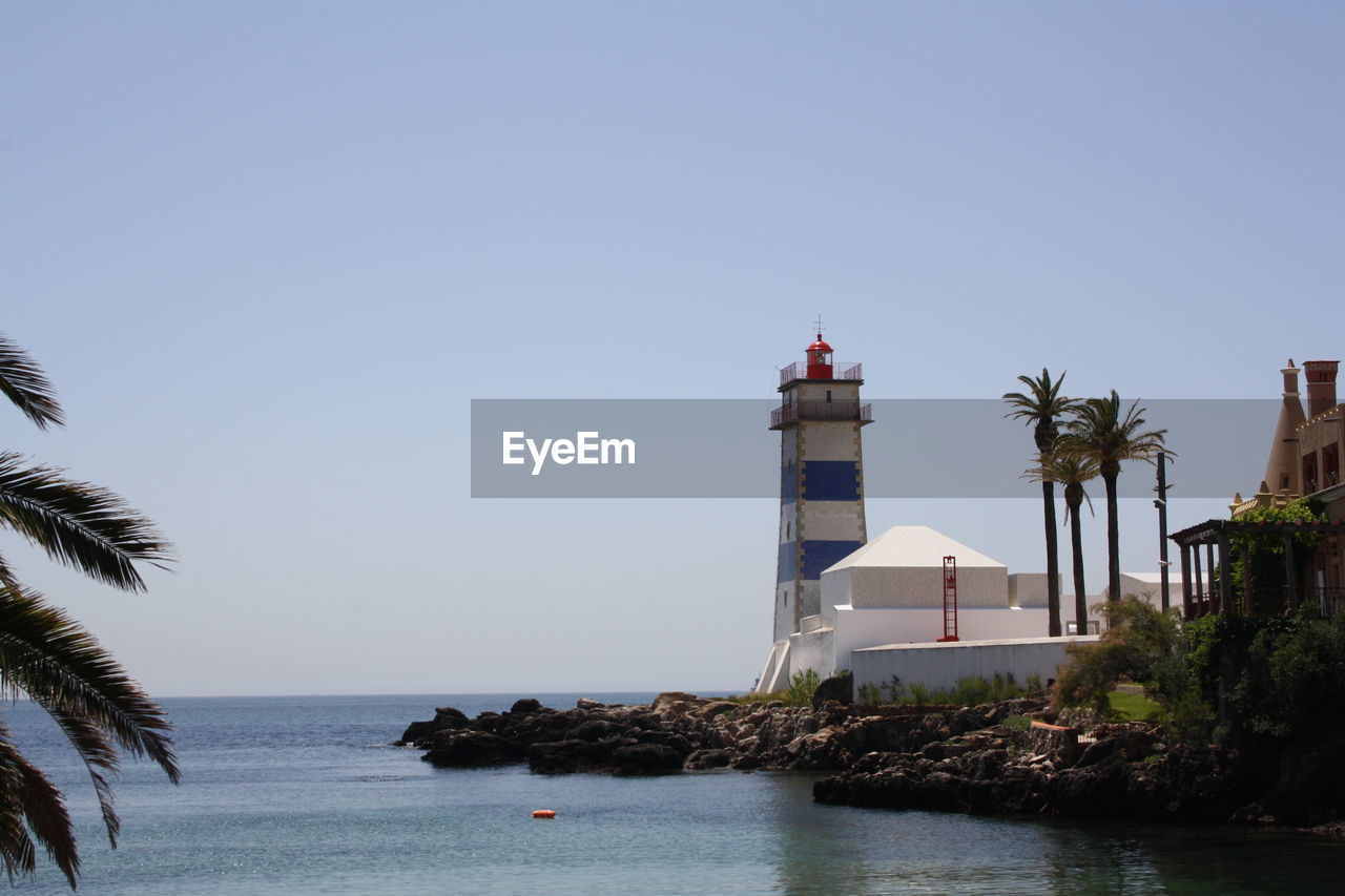 Lighthouse by sea against clear sky