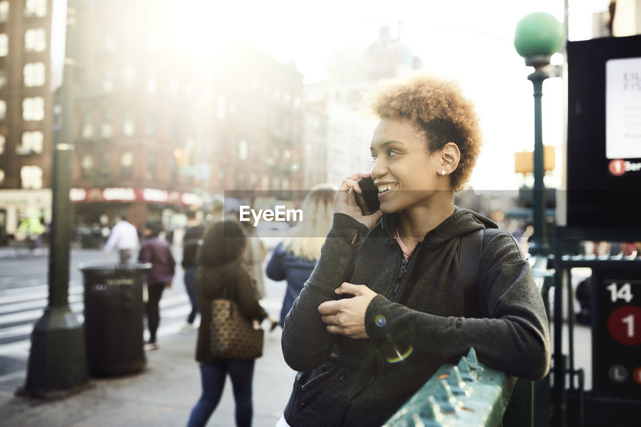 Happy young woman using smart phone on sidewalk during sunny day