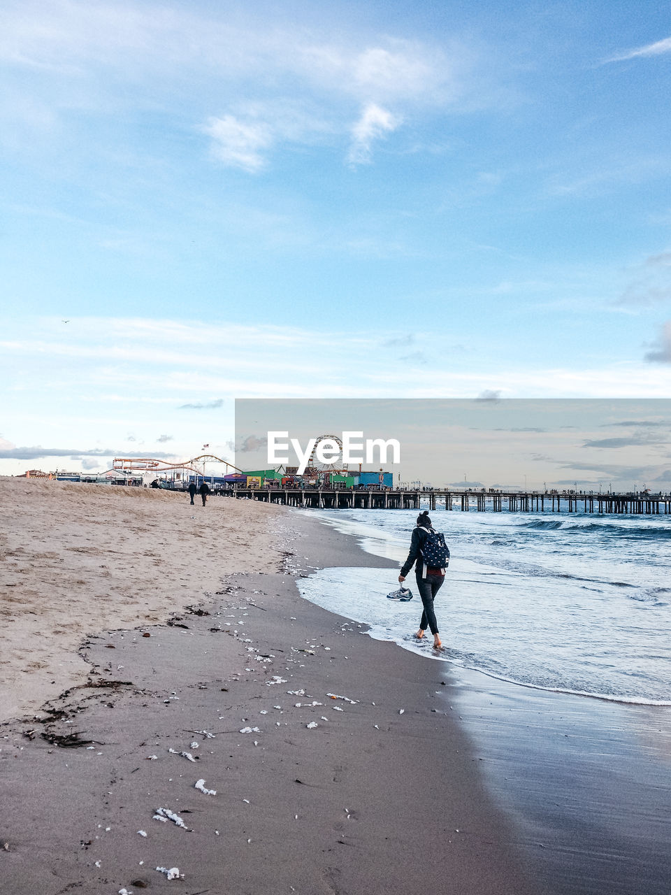 Woman walking on sea shore by amusement park against sky