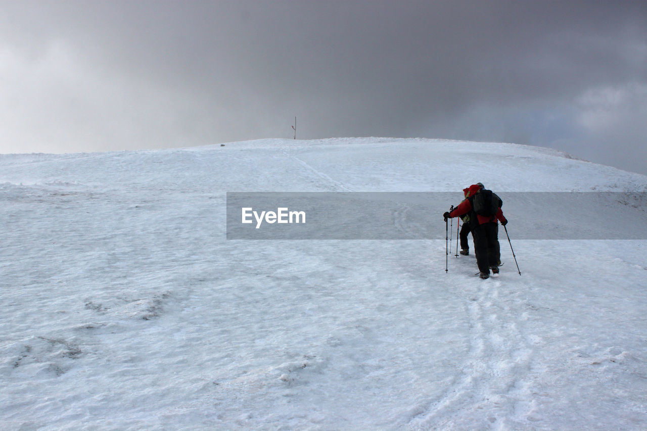 REAR VIEW OF MAN WALKING ON SNOW COVERED MOUNTAIN