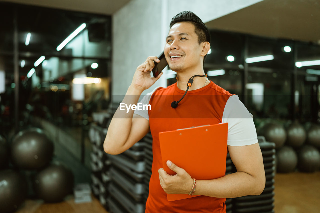 young woman using mobile phone while standing in gym