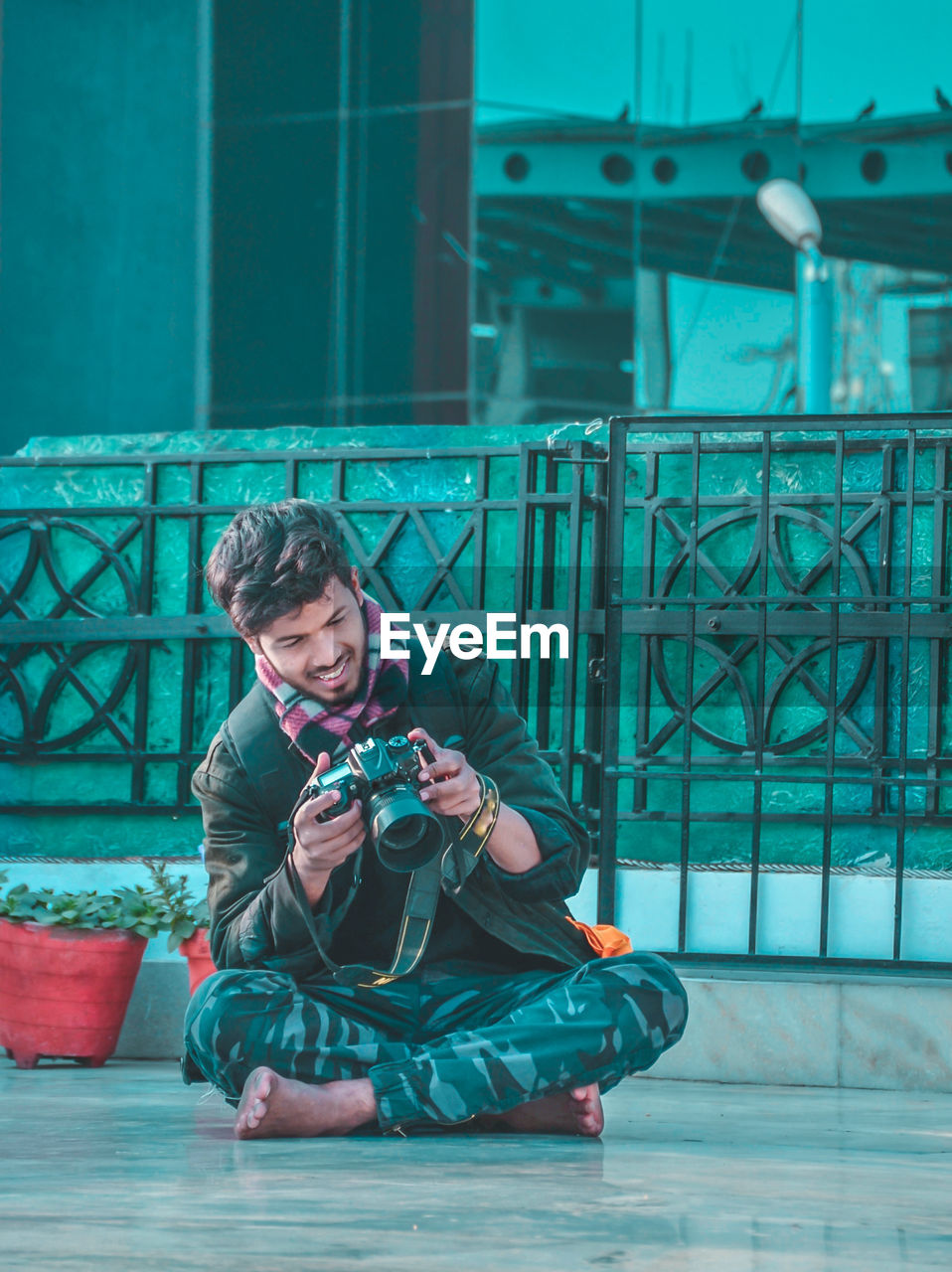 Full length of young man holding camera sitting outdoors