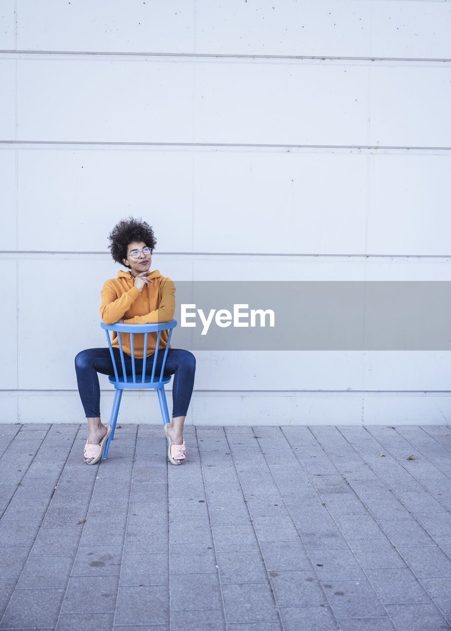 Thoughtful woman with hand on chin sitting in front of wall