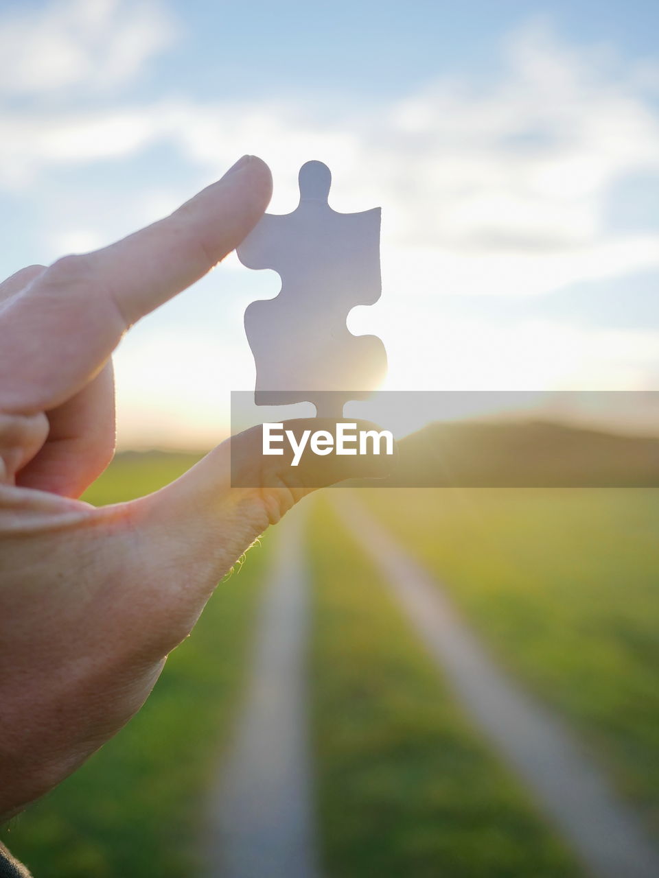 Cropped image of person holding jigsaw puzzle piece during sunset