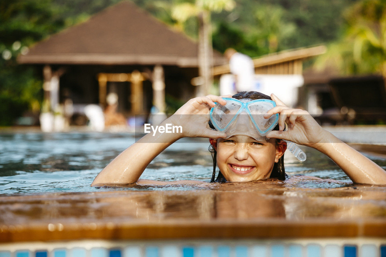 Portrait of smiling girl with swimming googles in pool at resort