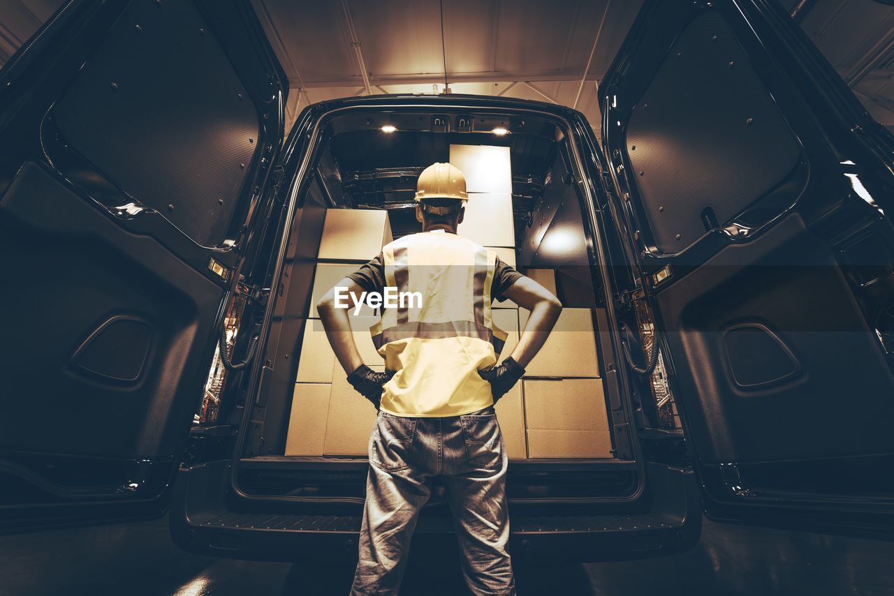 Rear view of delivery person standing by van with cardboard boxes