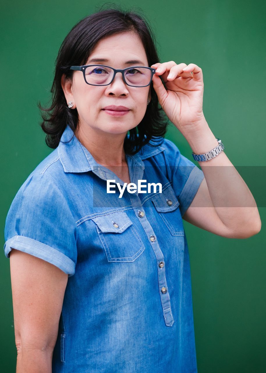 Portrait of confident teacher wearing eyeglasses against green chalkboard