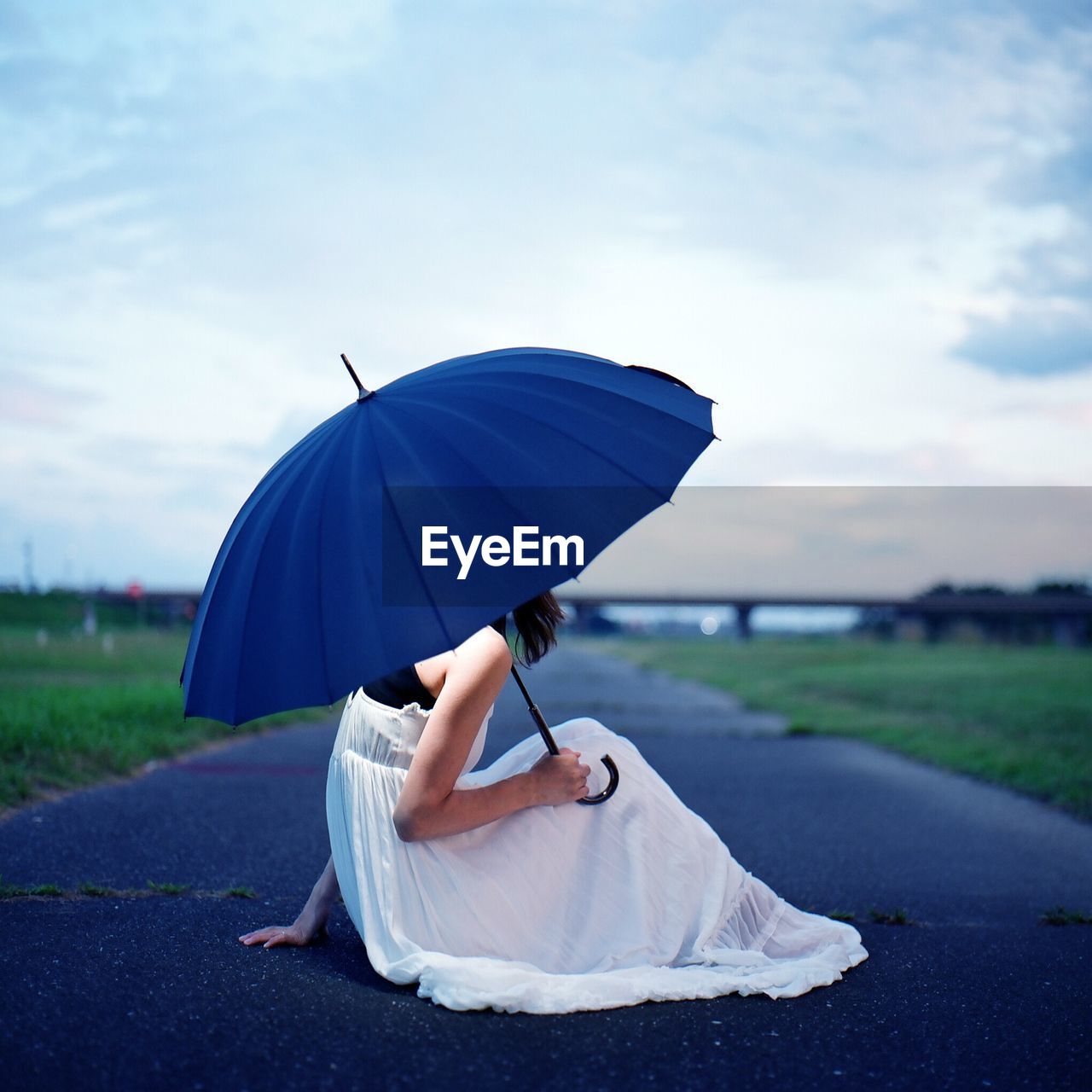 Side view of woman with umbrella sitting on road