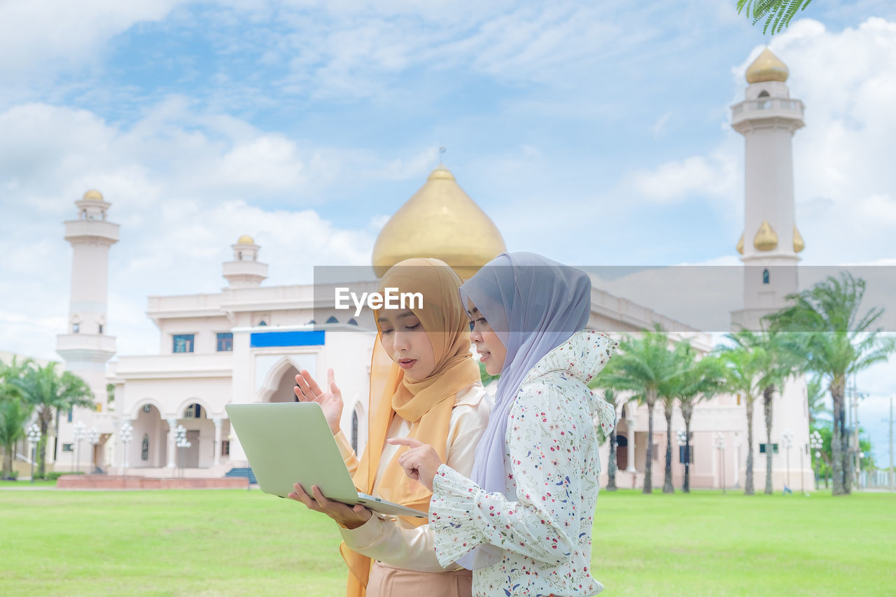 Young women using laptop against building