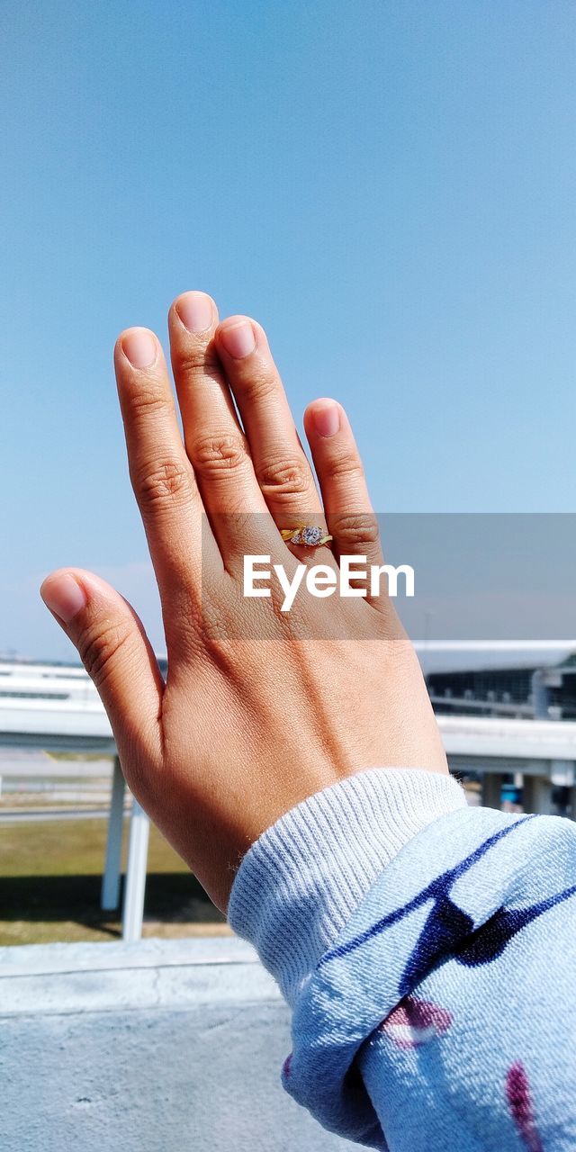 Cropped hand of woman with ring against clear sky