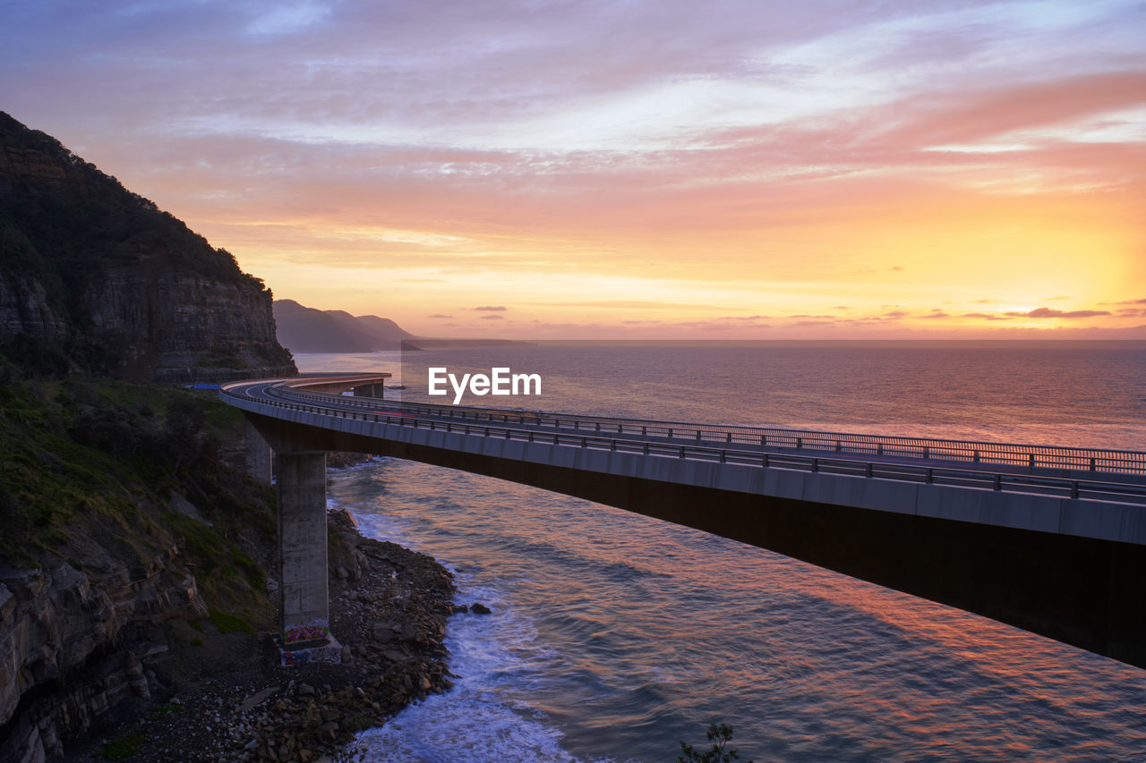 Bridge over sea against cloudy sky during sunrise