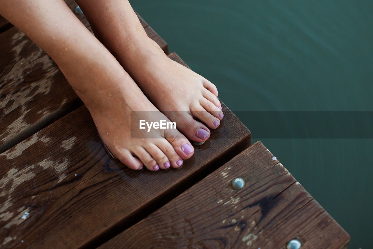 Low section of woman relaxing on pier over lake