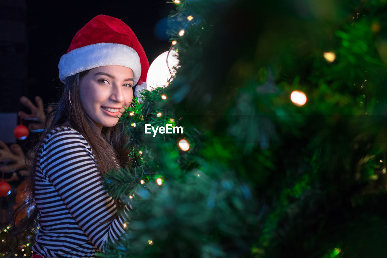 Portrait of smiling woman by illuminated christmas tree at night