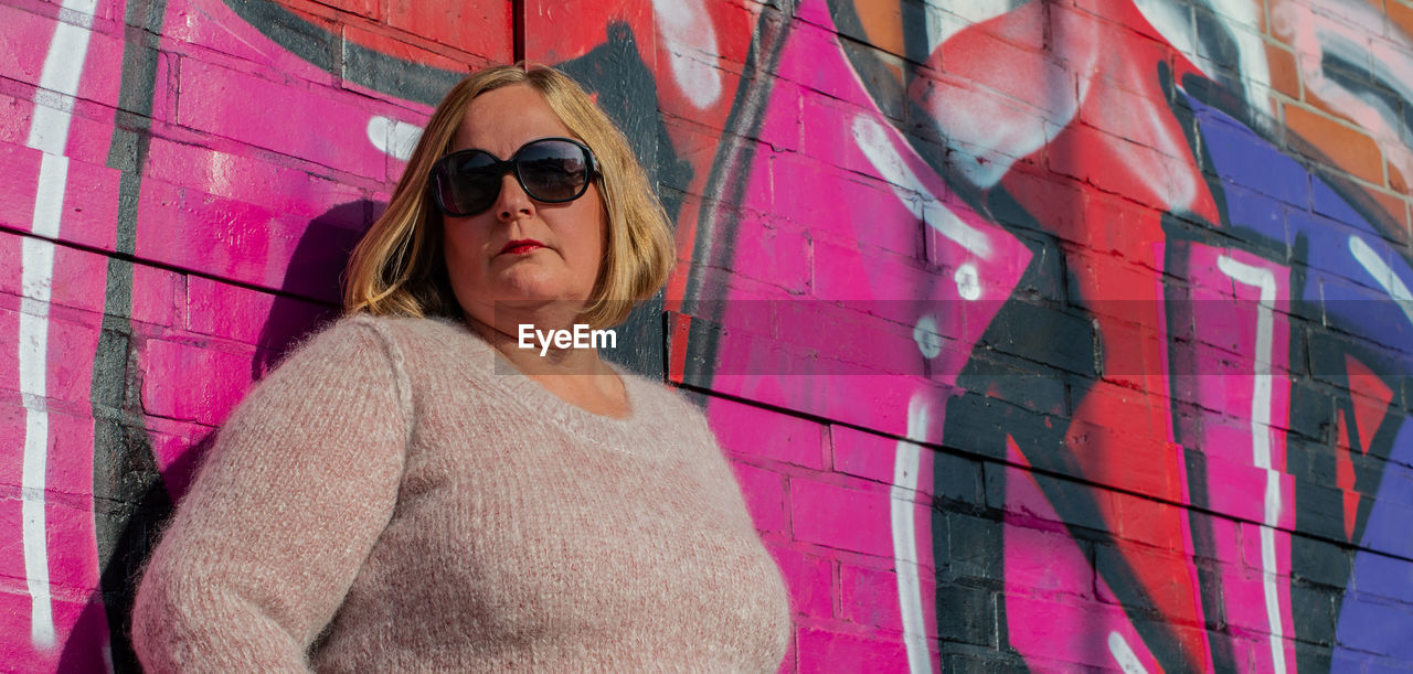 PORTRAIT OF WOMAN STANDING AGAINST WALL