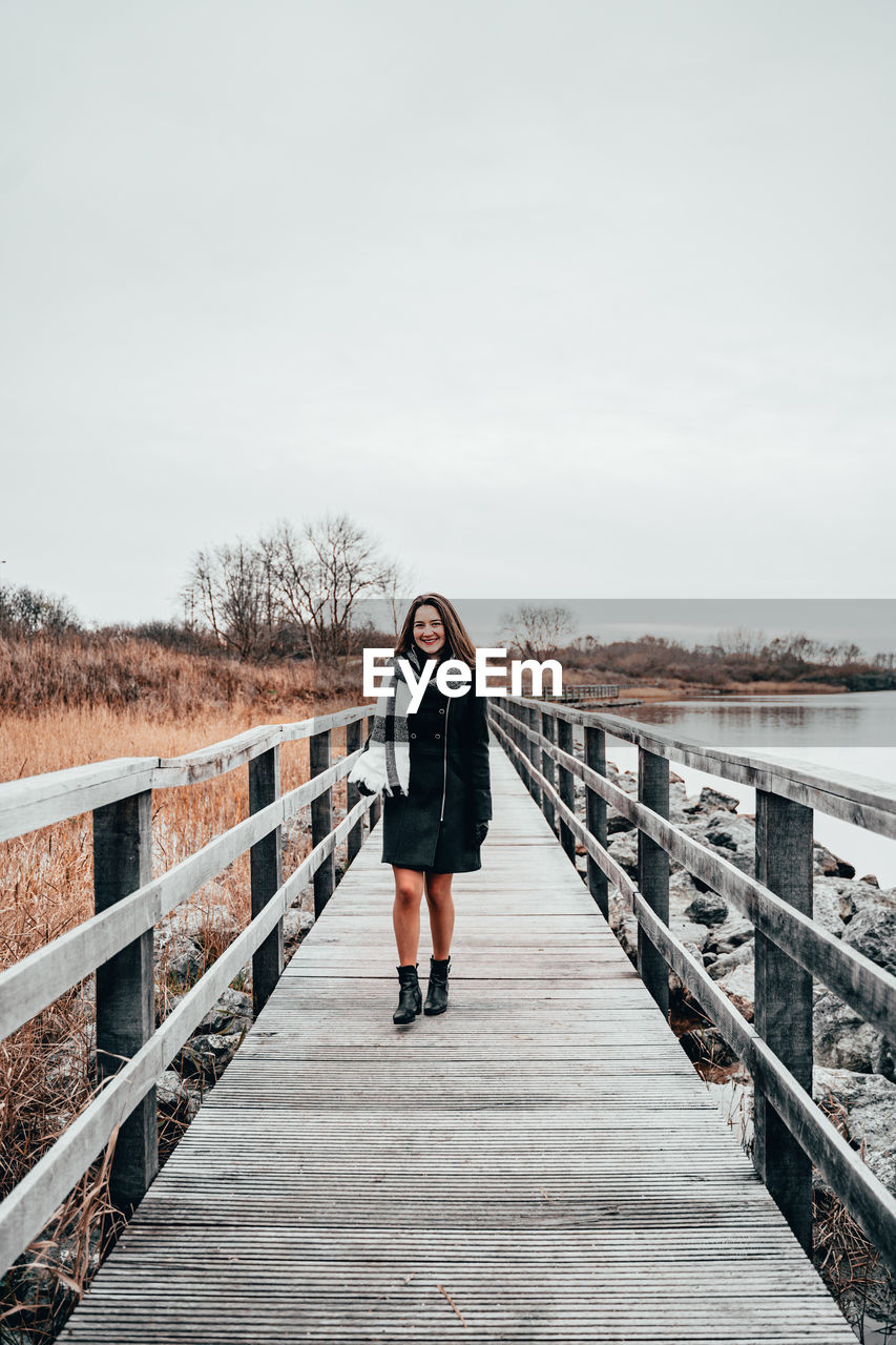 Portrait of woman walking on footbridge against sky