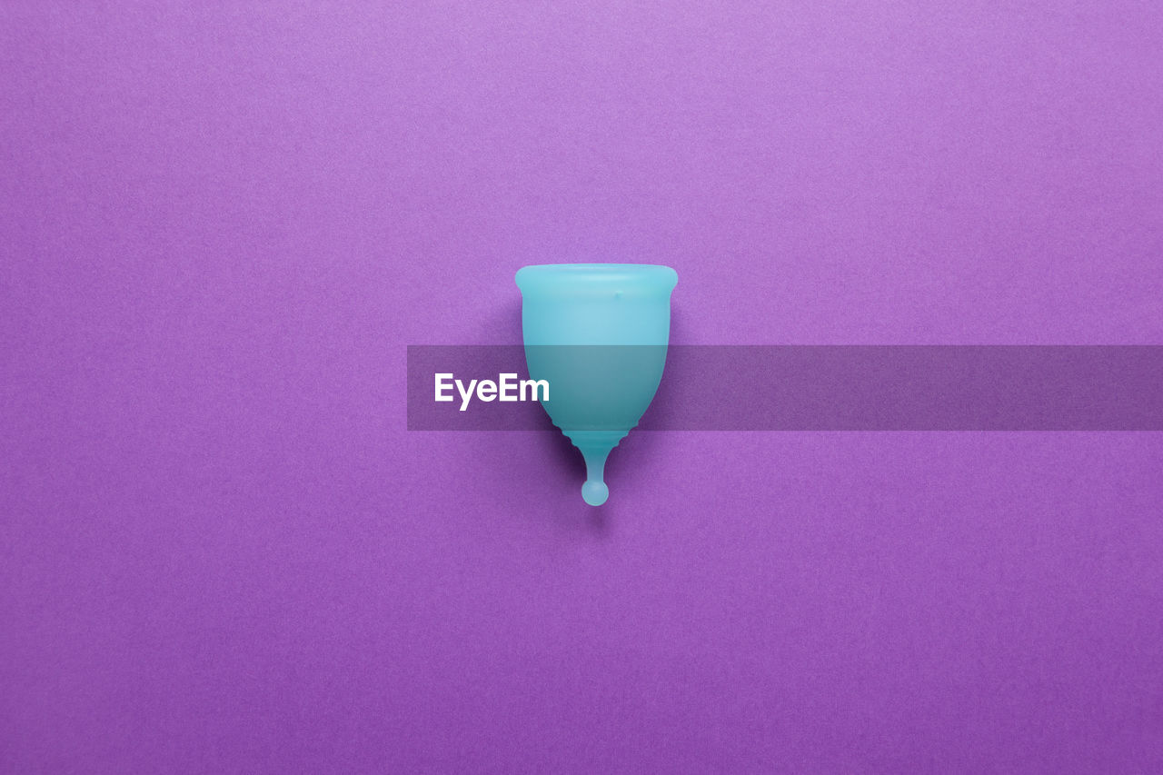 Turquoise menstrual cup on purple background. concept zero waste living, savings, minimalism