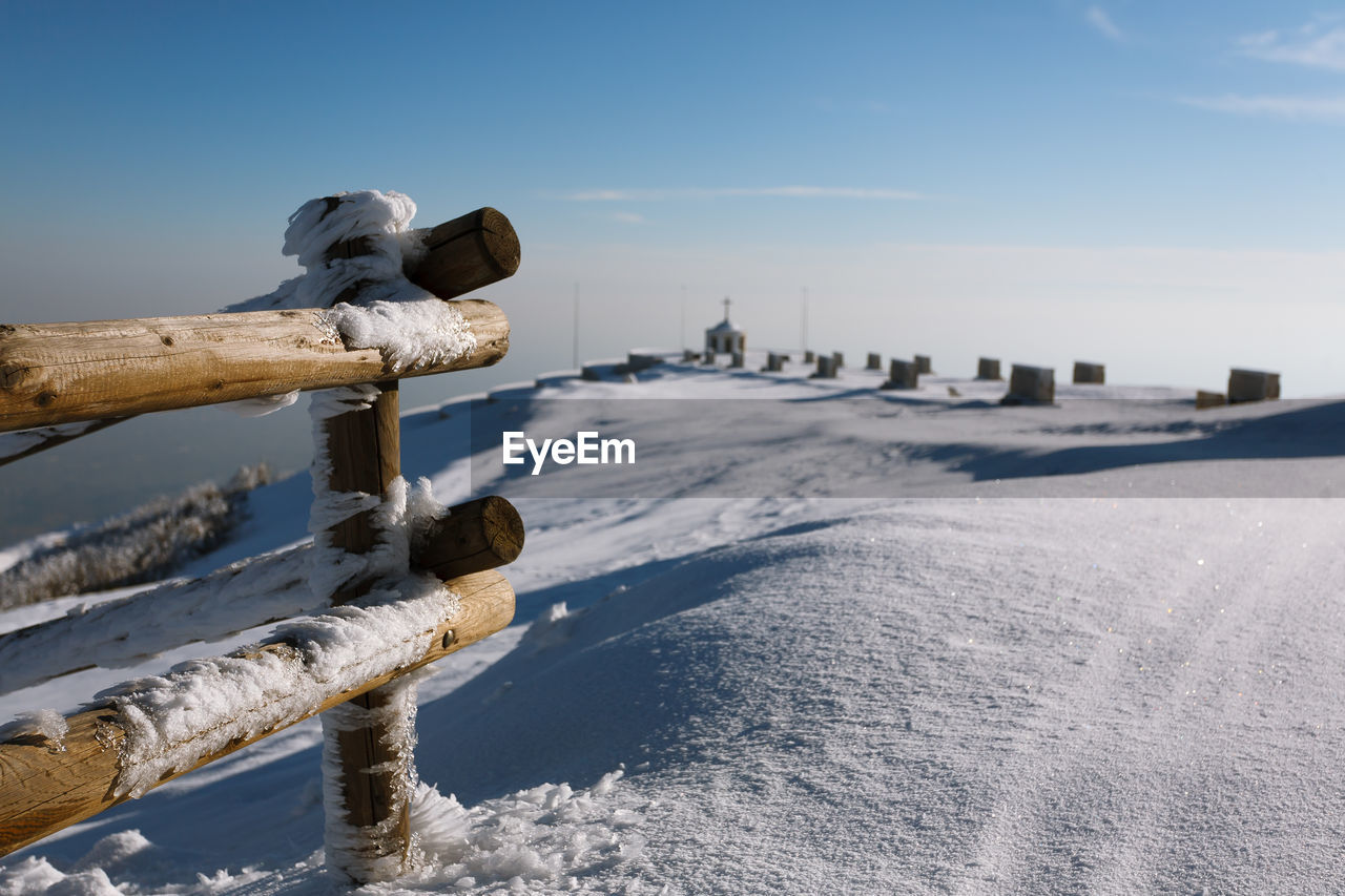 SNOW COVERED WOODEN POST ON LAND AGAINST SKY