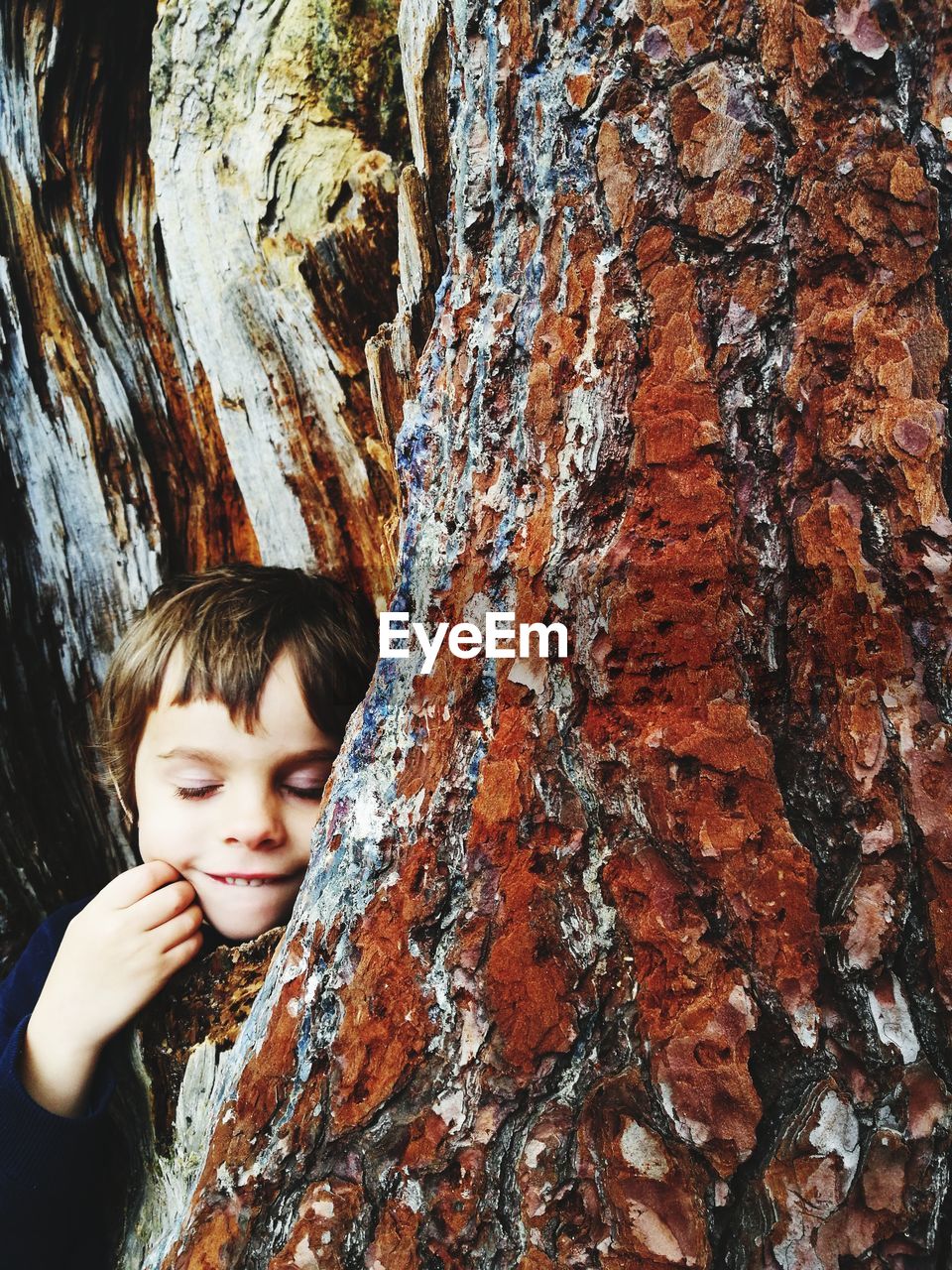 Cute boy leaning on tree trunk