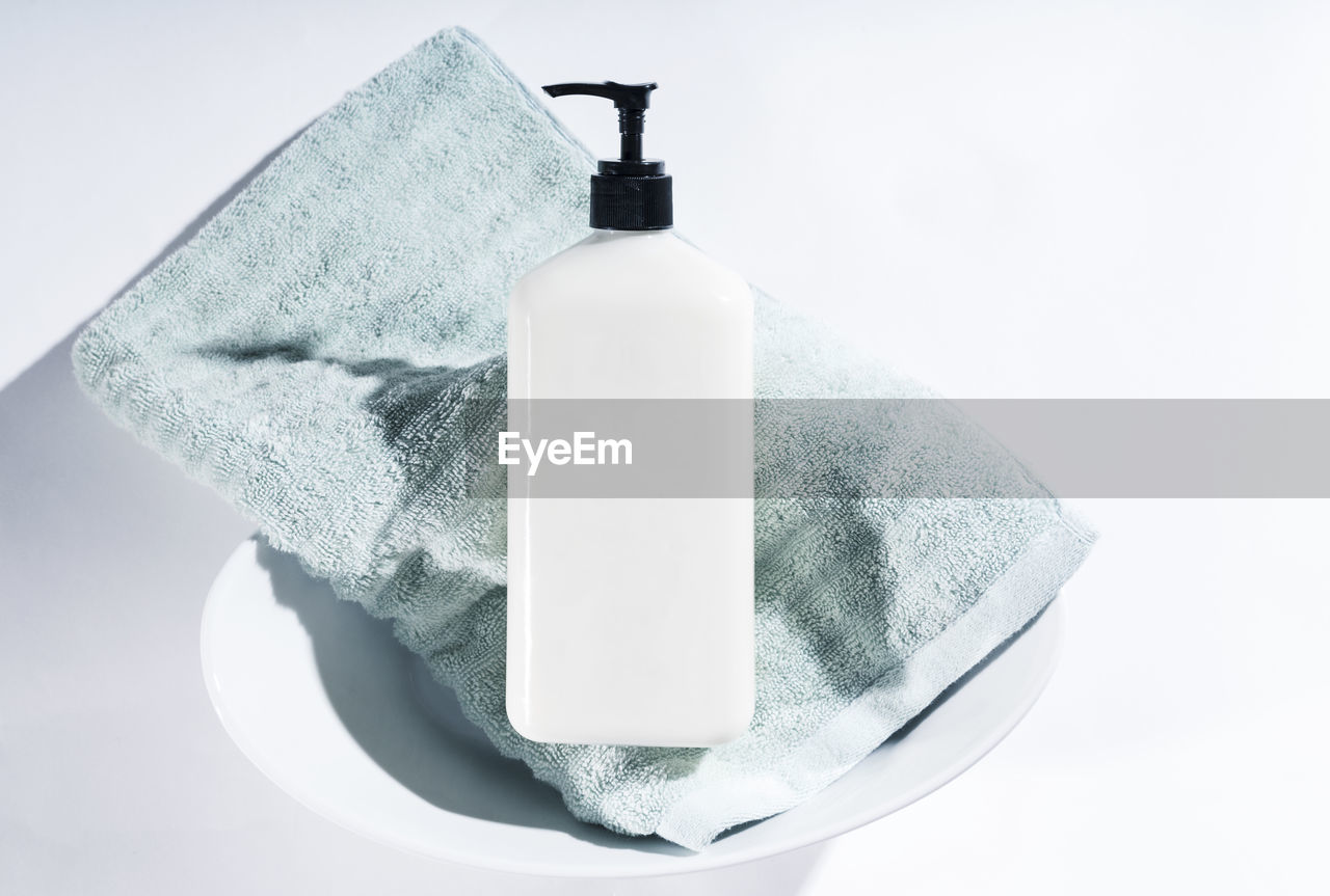 Close-up of soap dispenser with towel over white background