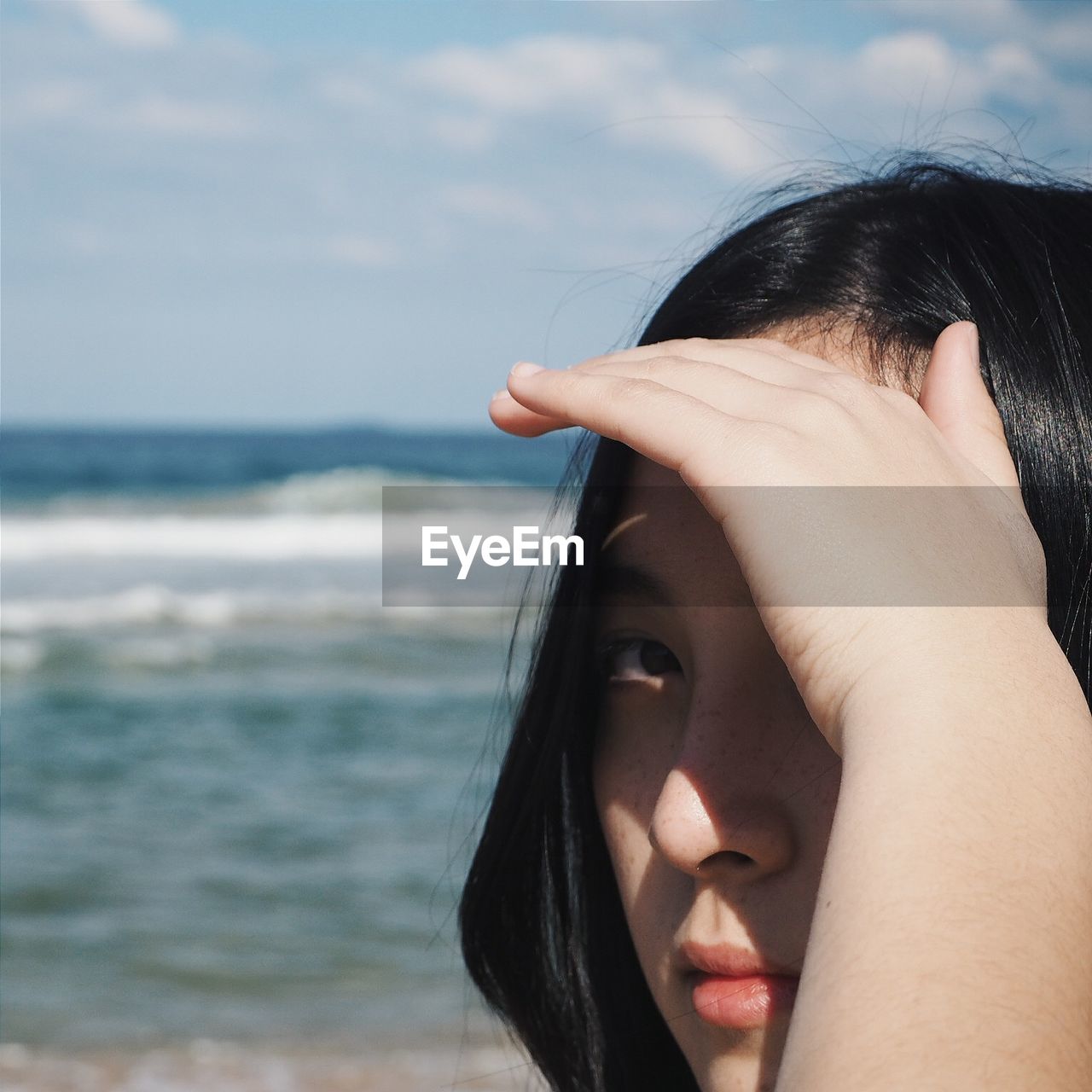 Close-up portrait of woman shielding eyes while standing at beach