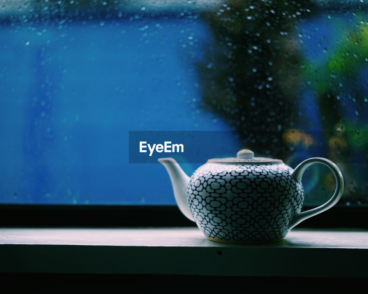 CLOSE-UP OF COFFEE CUP ON WINDOW SILL IN FRONT OF BLUE GLASS