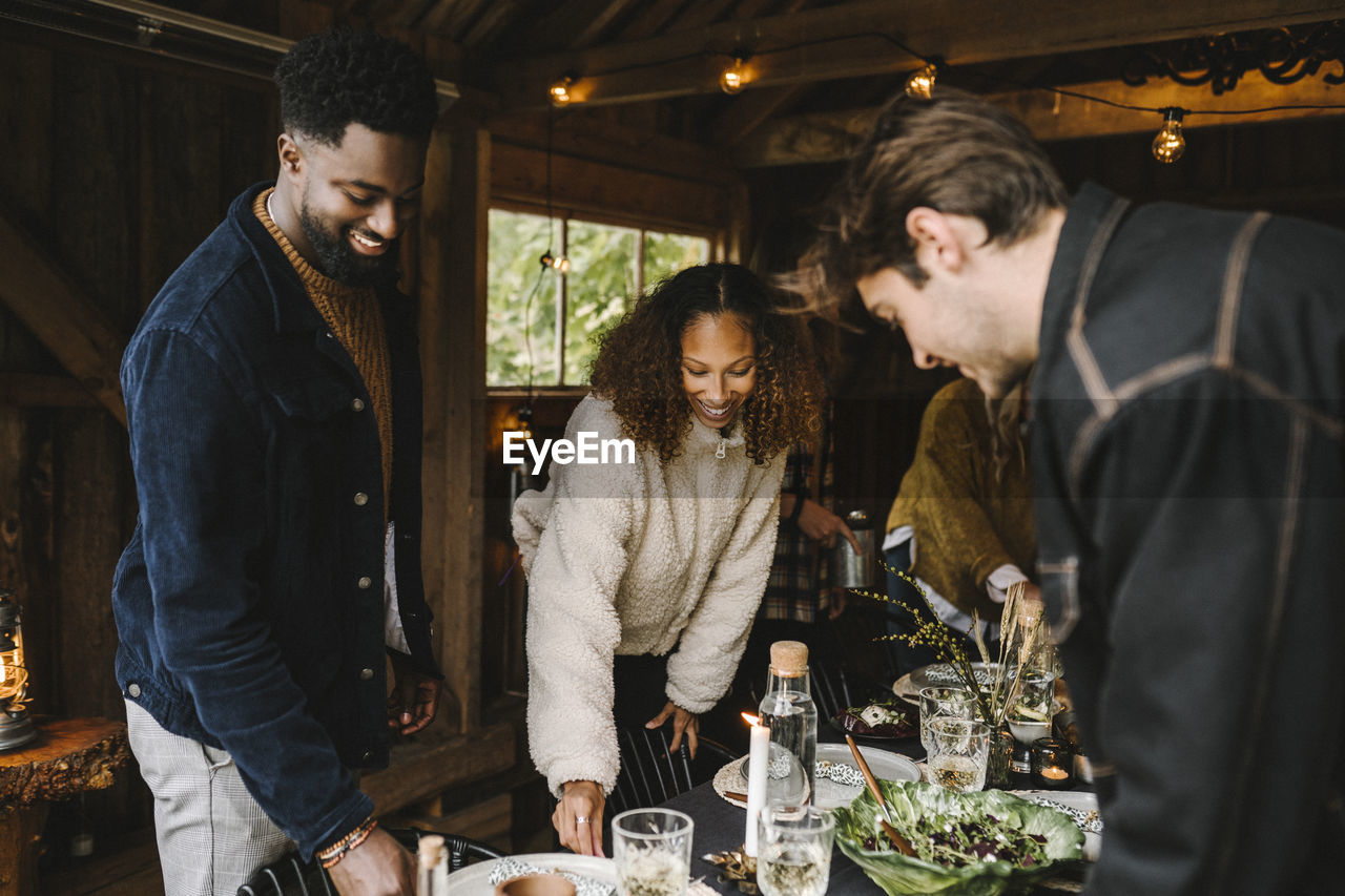 Side view of man with smiling friends arranging dining table for social gathering