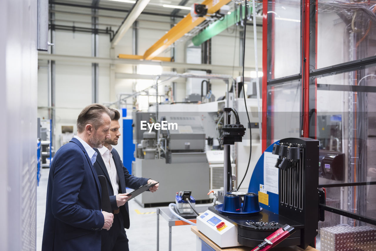 Two businessmen in factory shop floor examining machine