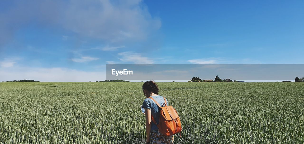 REAR VIEW OF WOMAN STANDING IN FIELD