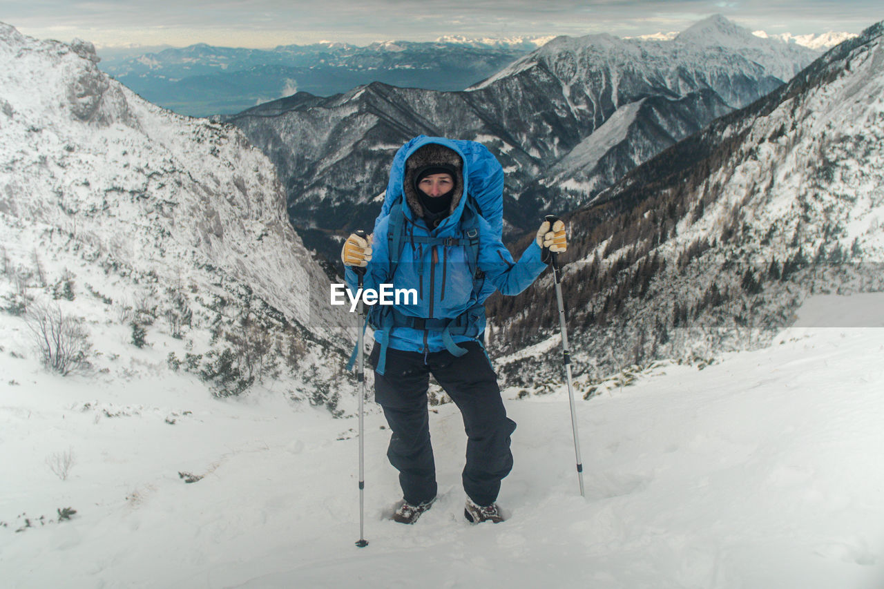 Woman hiking uphill on snowcapped mountain against sky