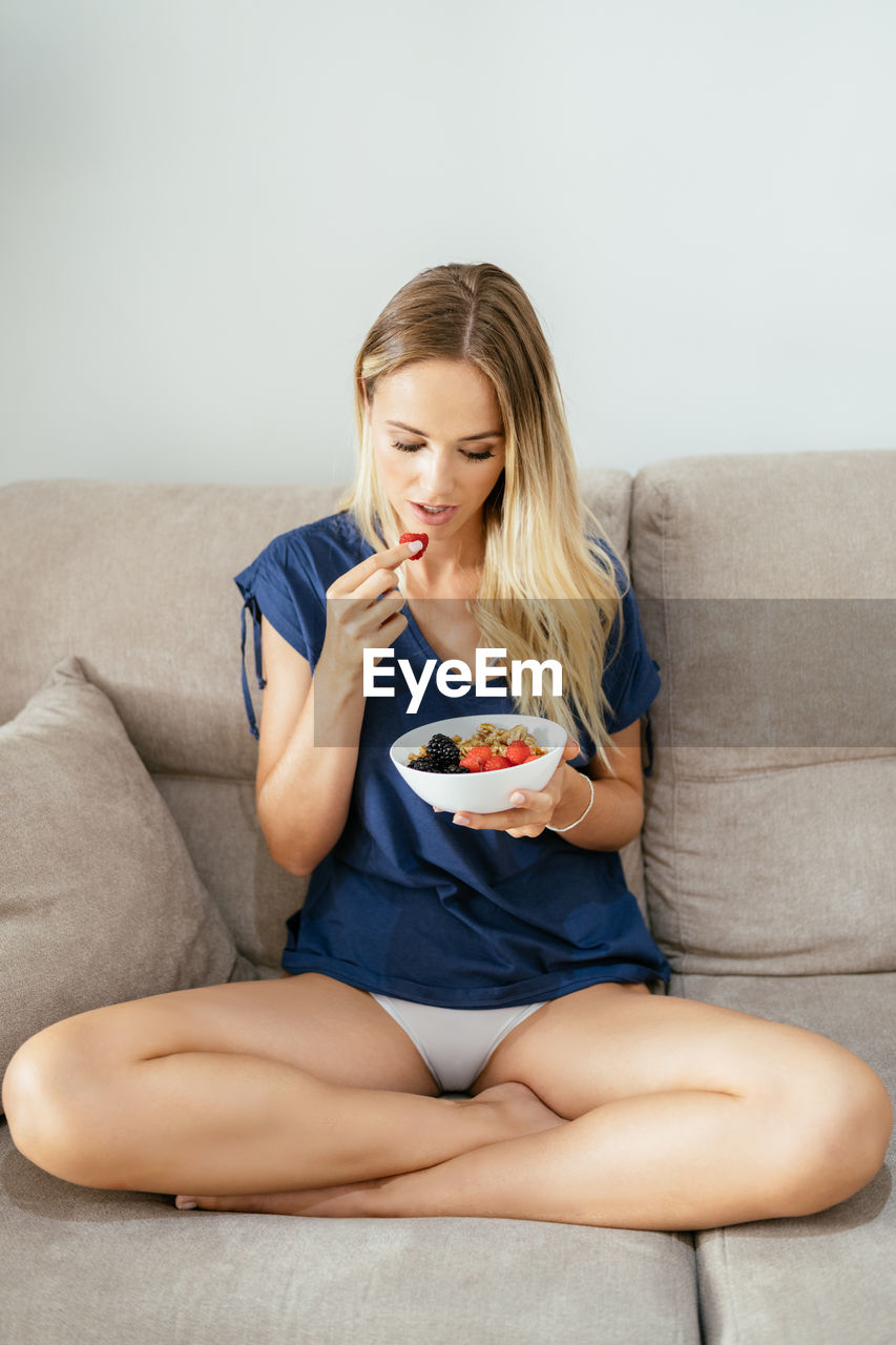 Young woman eating fruits sitting on sofa at home