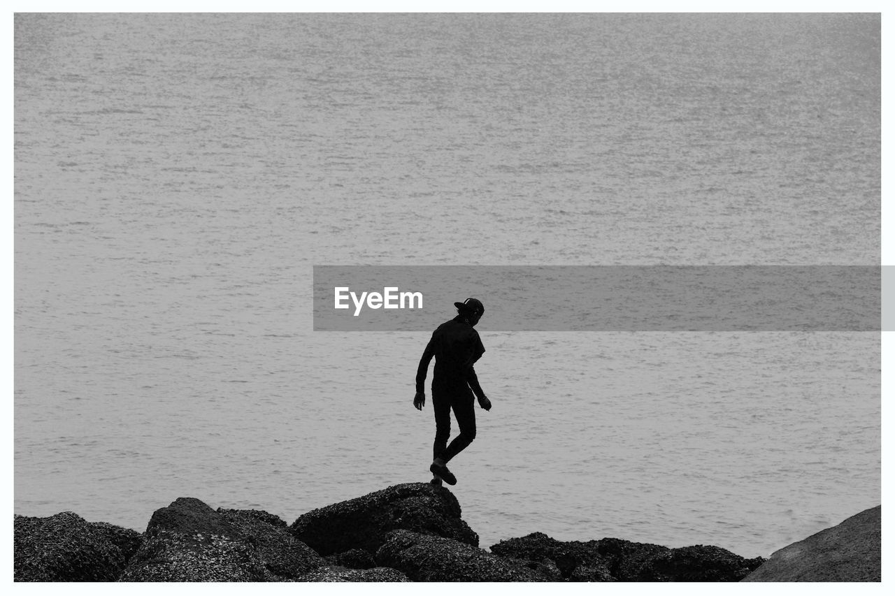 Silhouette man walking on rock formation by sea