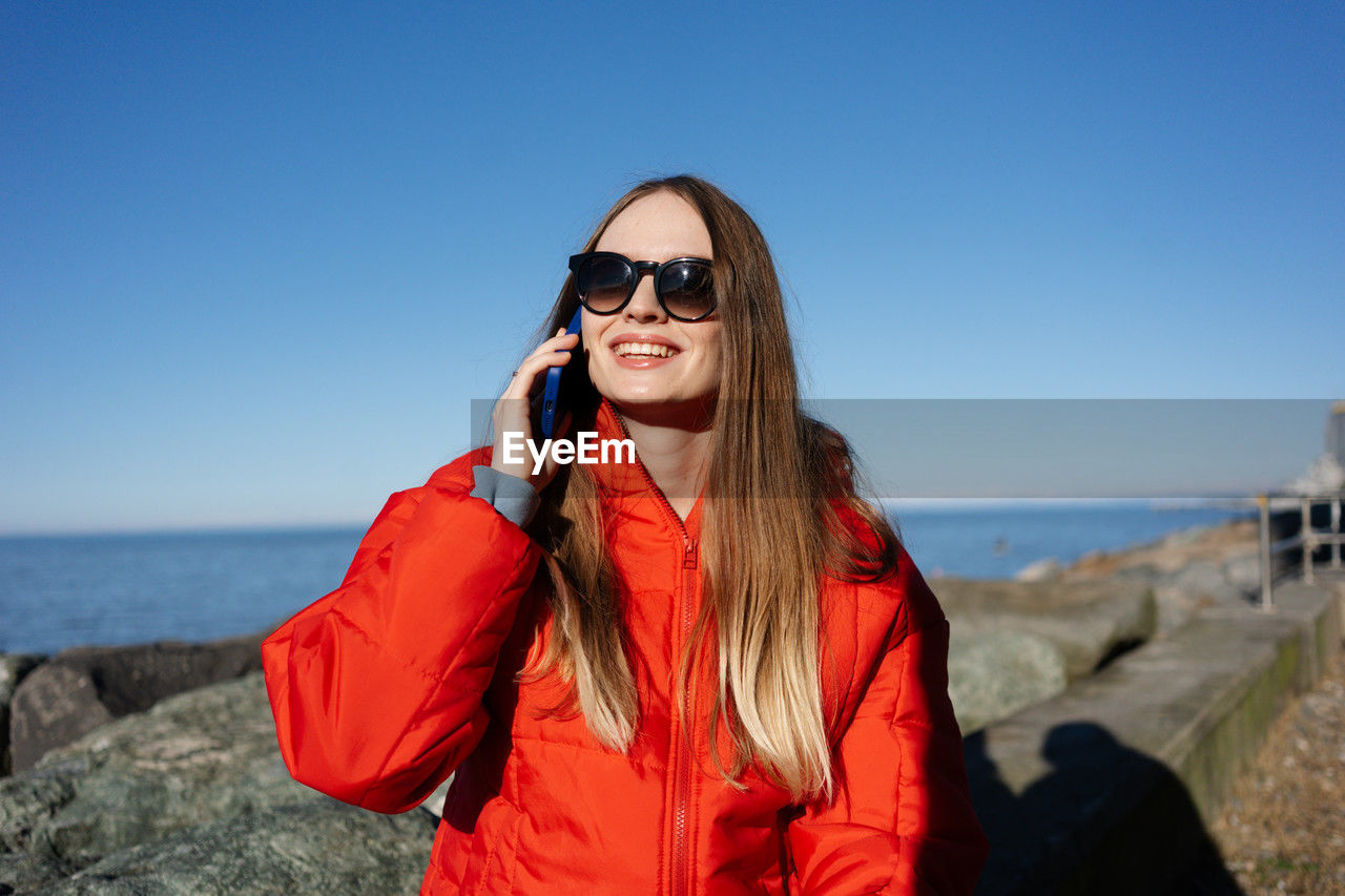 Happy woman in red jacket against sea background talking on phone. calls abroad. high quality photo