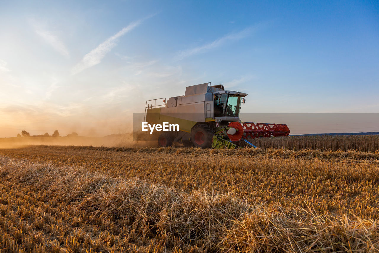 Tractor harvesting on agricultural field against sky