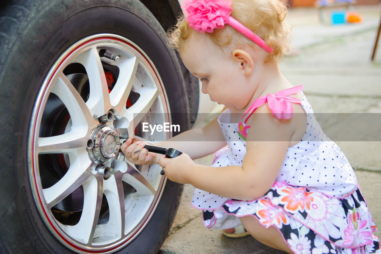 Full length of cute girl holding tool by car