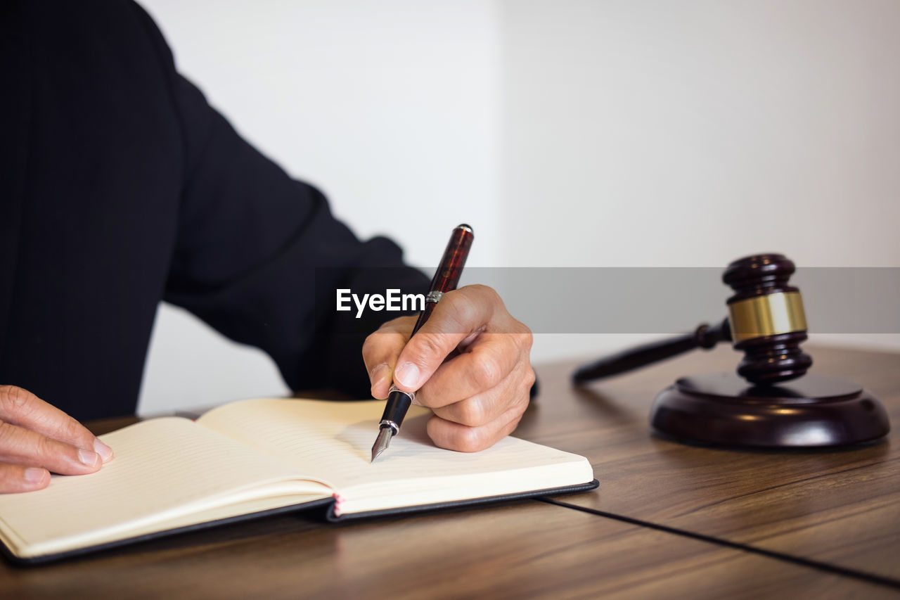 Midsection of lawyer writing in book at desk