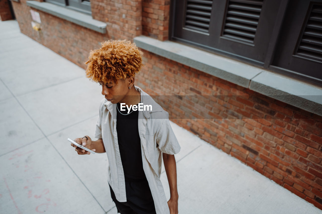 Portrait view of the multiracial man typing sms while standing near the brick wall