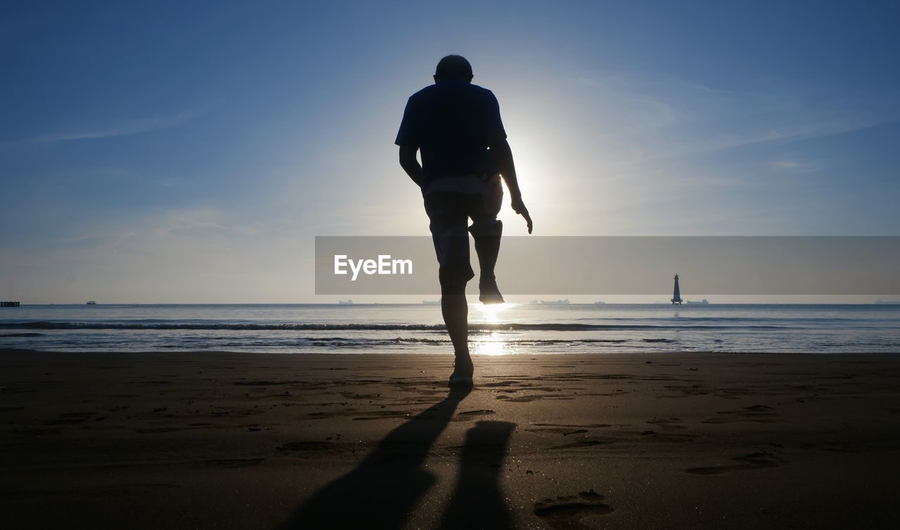 Rear view of silhouette man standing on one leg at beach