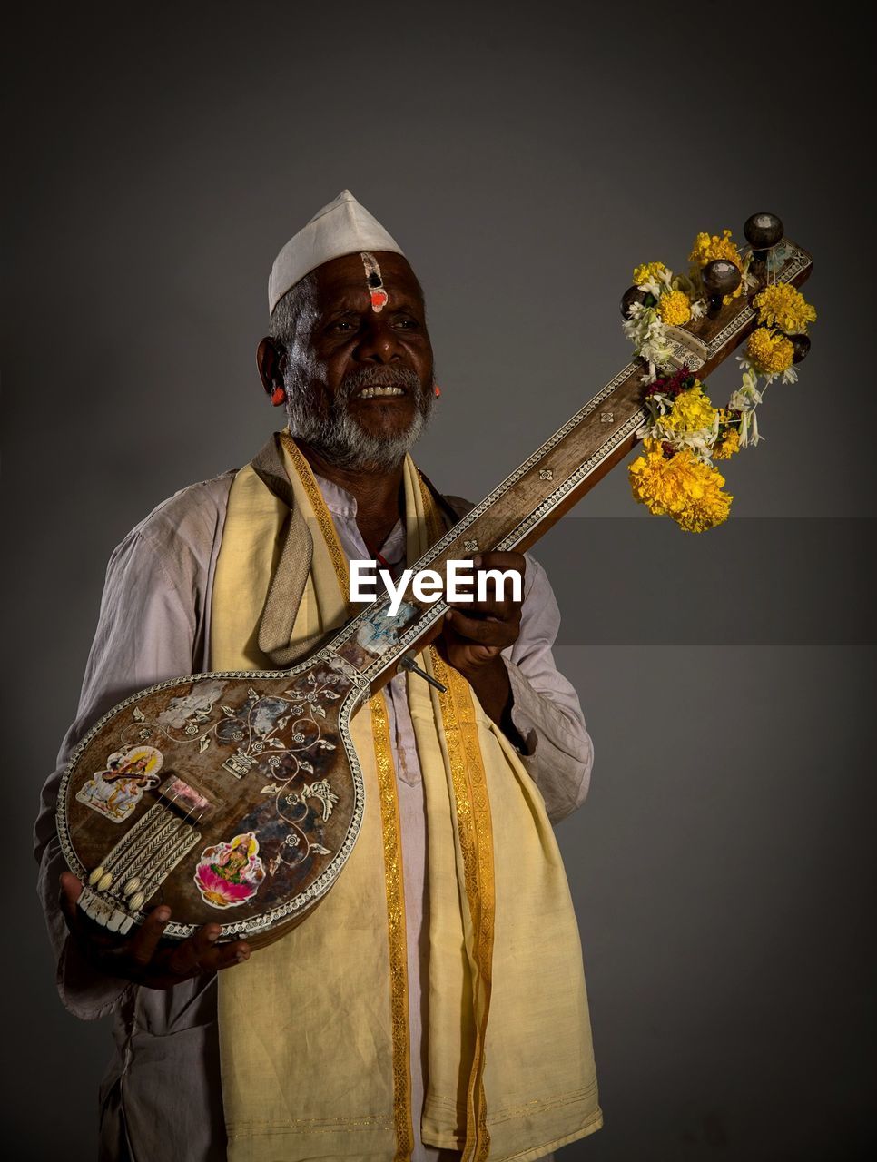 Smiling mature man holding musical instrument against gray background