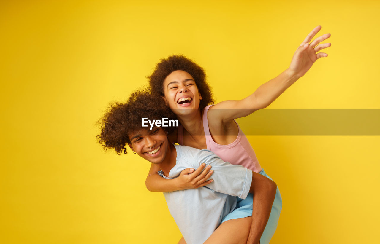 portrait of young woman with arms raised against yellow background