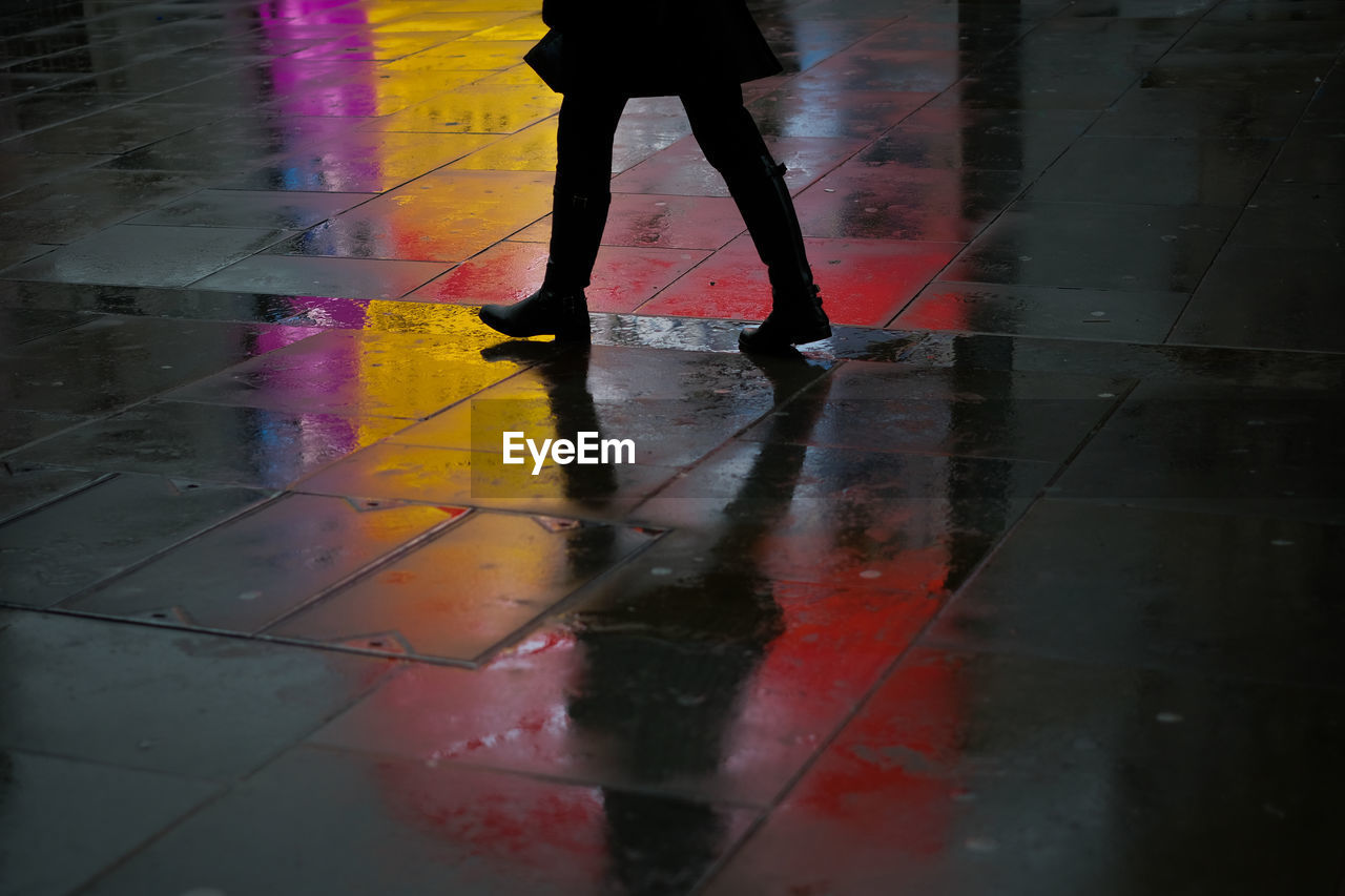 Low section of woman walking on wet footpath in city at night