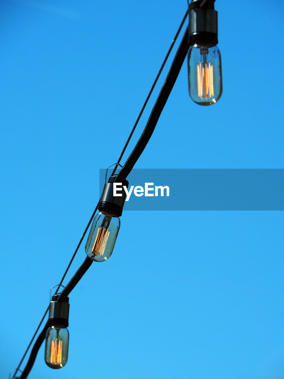 Low angle view of light bulbs against clear blue sky