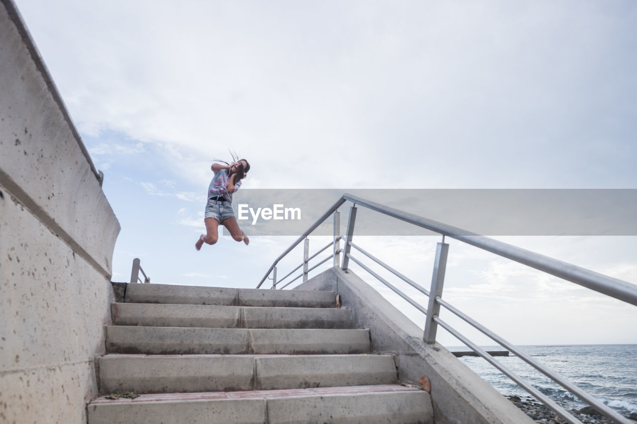 Full length of woman jumping on staircase against sky