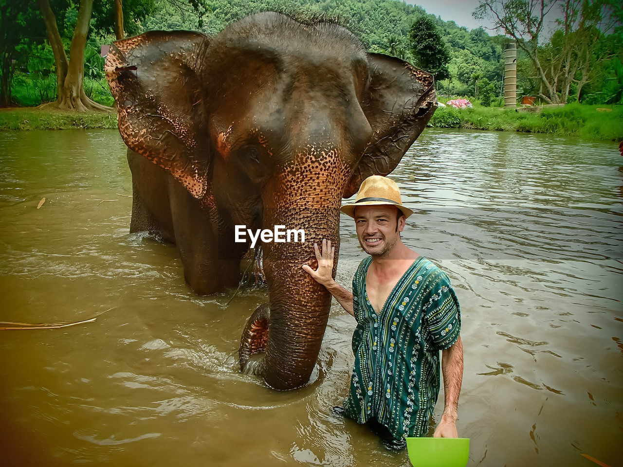Portrait of man standing by elephant in lake