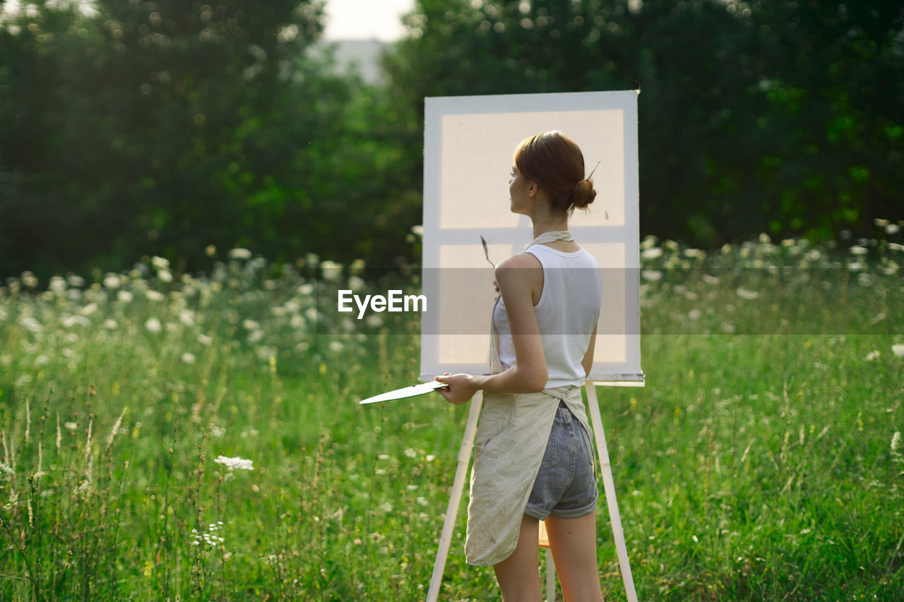 REAR VIEW OF WOMAN STANDING ON FIELD AGAINST TREES